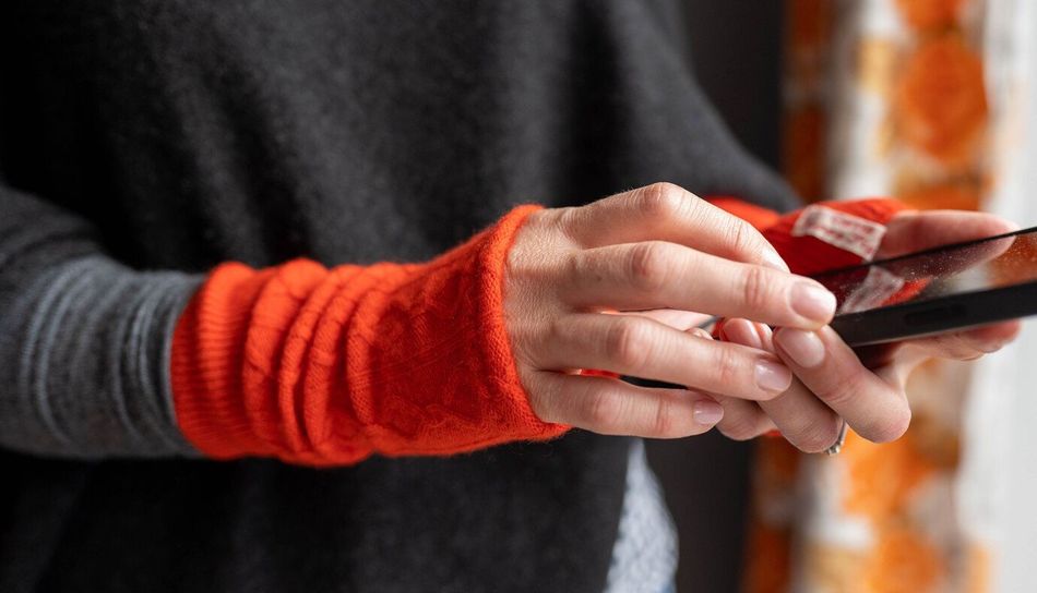 Hands holding a phone, wearing orange cable knit cashmere wrist warmers