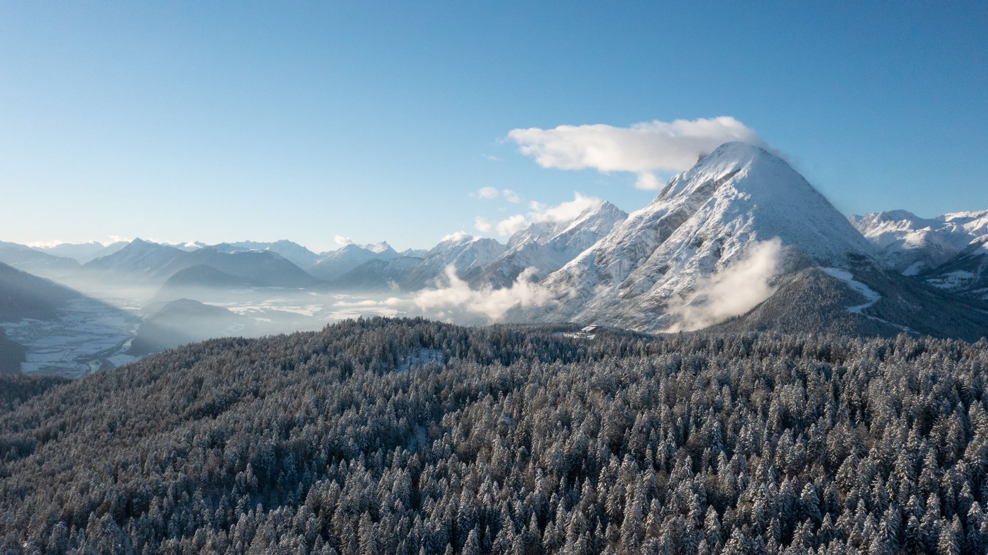 Eine Luftaufnahme einer schneebedeckten Bergkette mit einem Wald im Vordergrund.