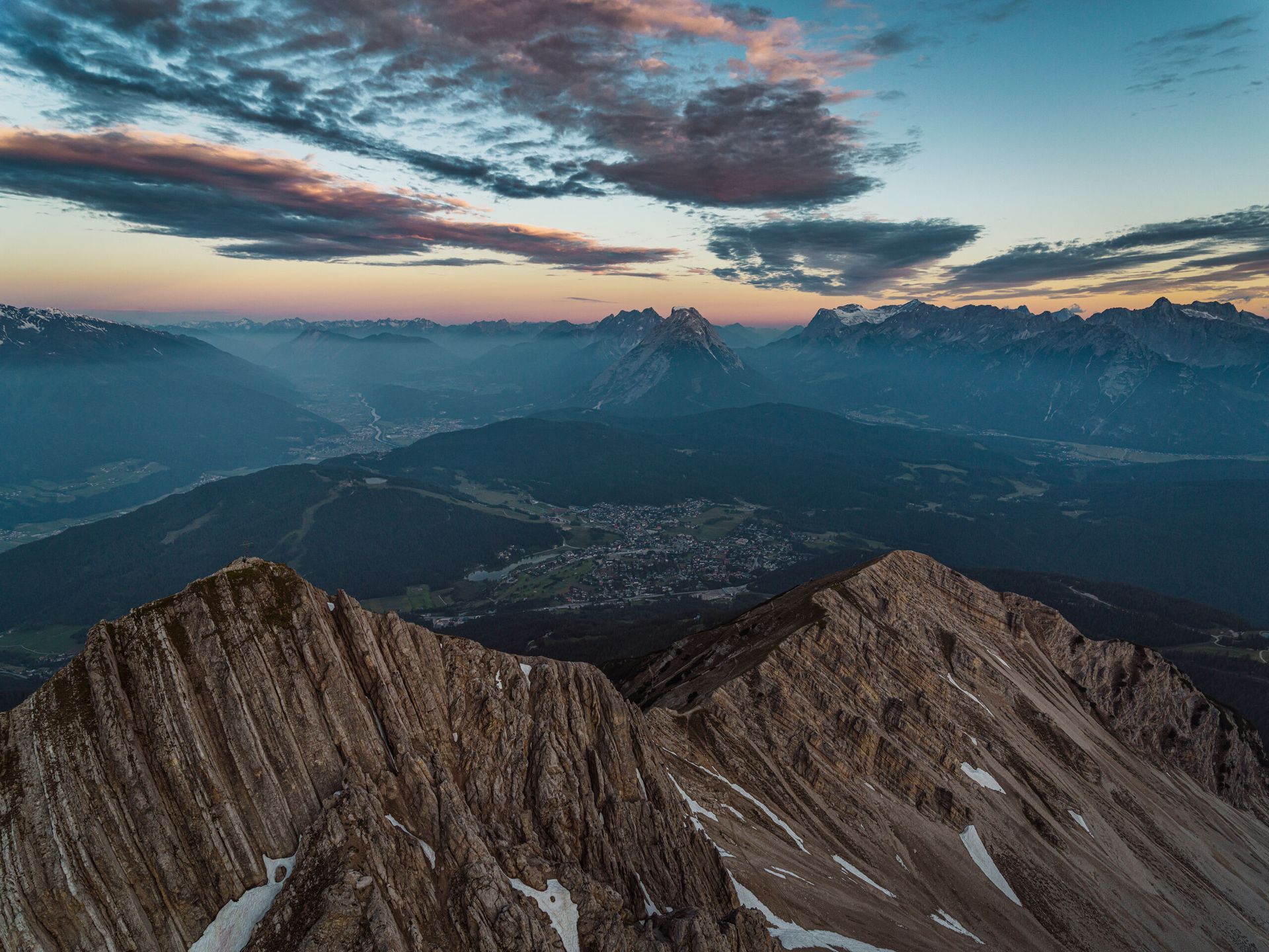 Eine Luftaufnahme einer Bergkette bei Sonnenuntergang mit einer Stadt in der Ferne.