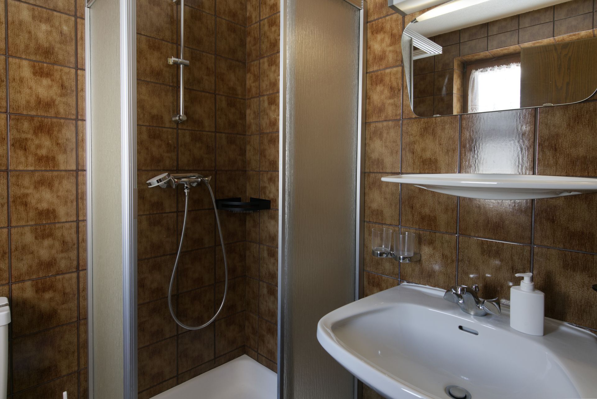 Een badkamer met wastafel, douche en spiegel.