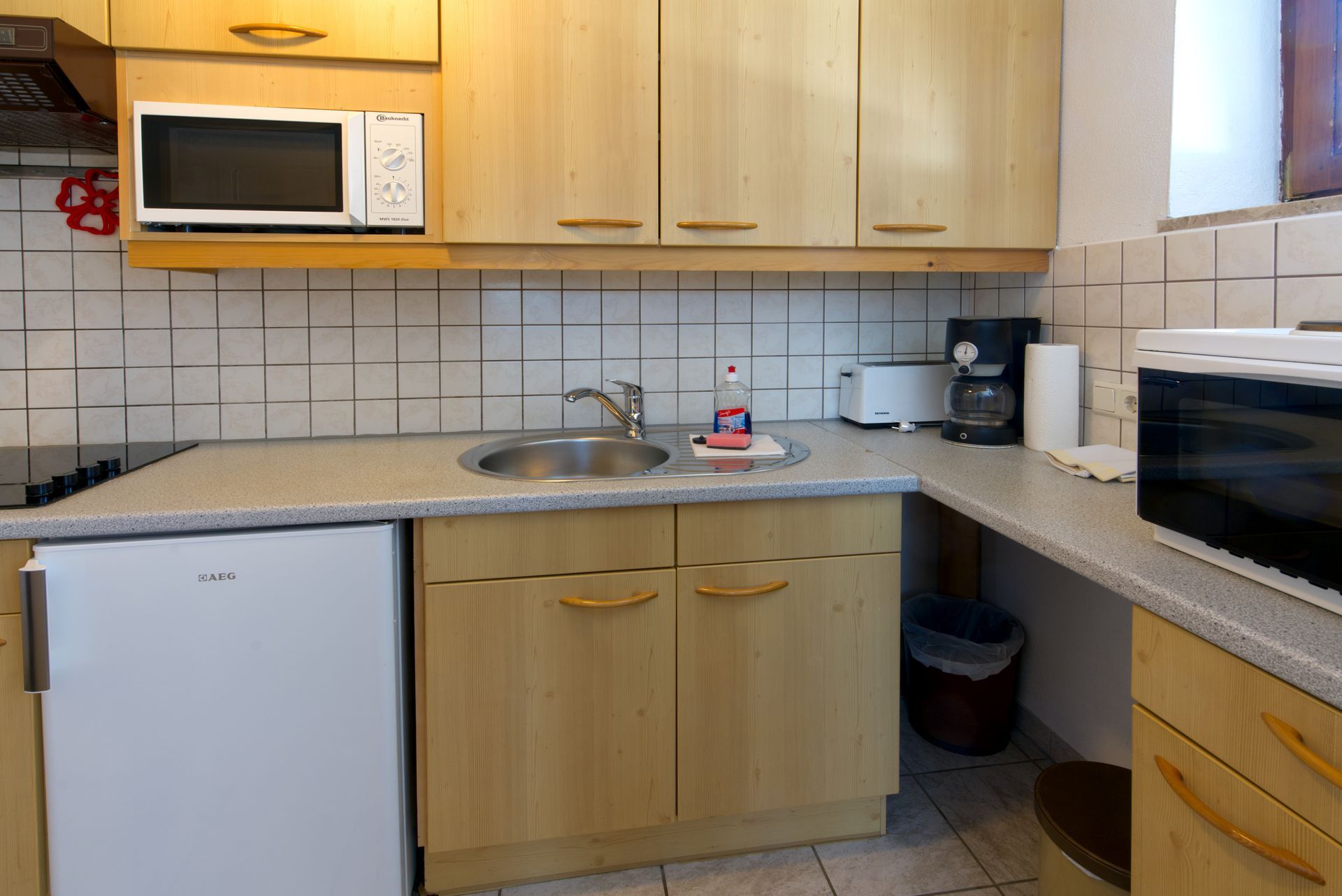 Een keuken met houten kasten, een gootsteen, een magnetron en een koelkast.