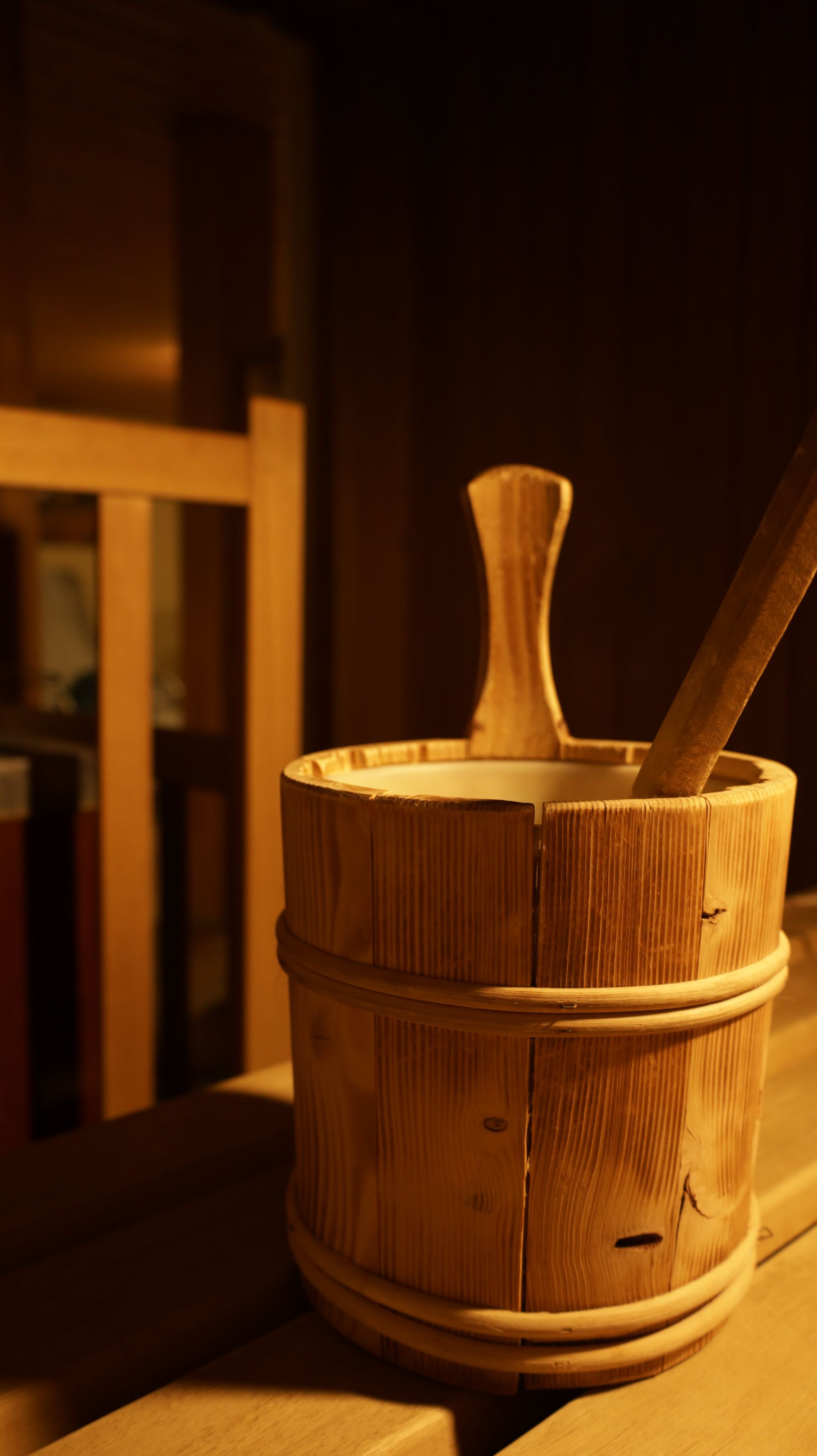 Een houten emmer met een houten lepel erin staat op een houten bankje in een sauna.