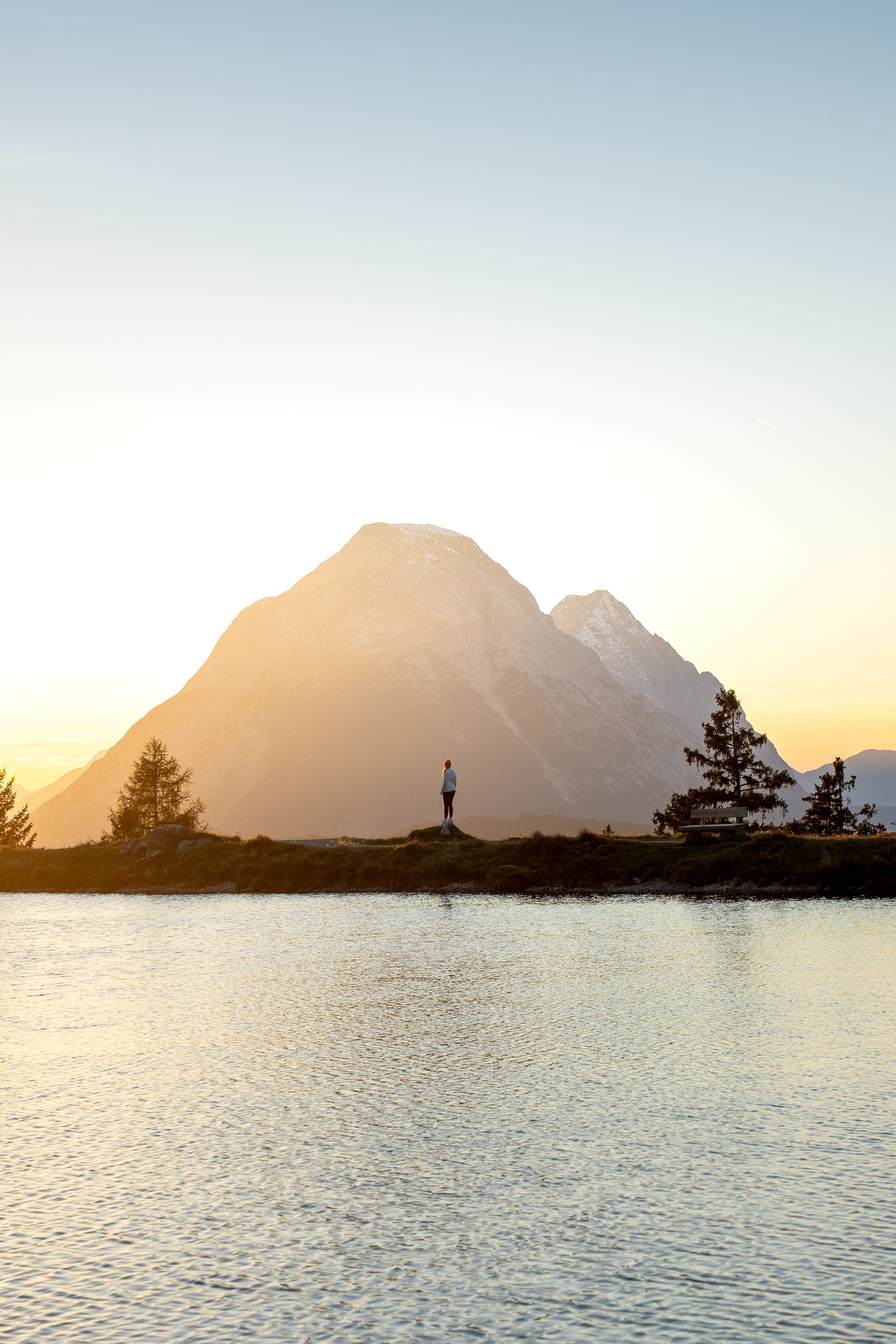 Ein See mit einem Berg im Hintergrund bei Sonnenuntergang