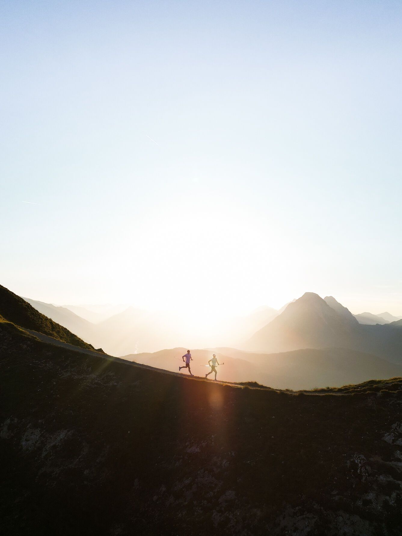 Zwei Leute laufen bei Sonnenuntergang auf einem Hügel.