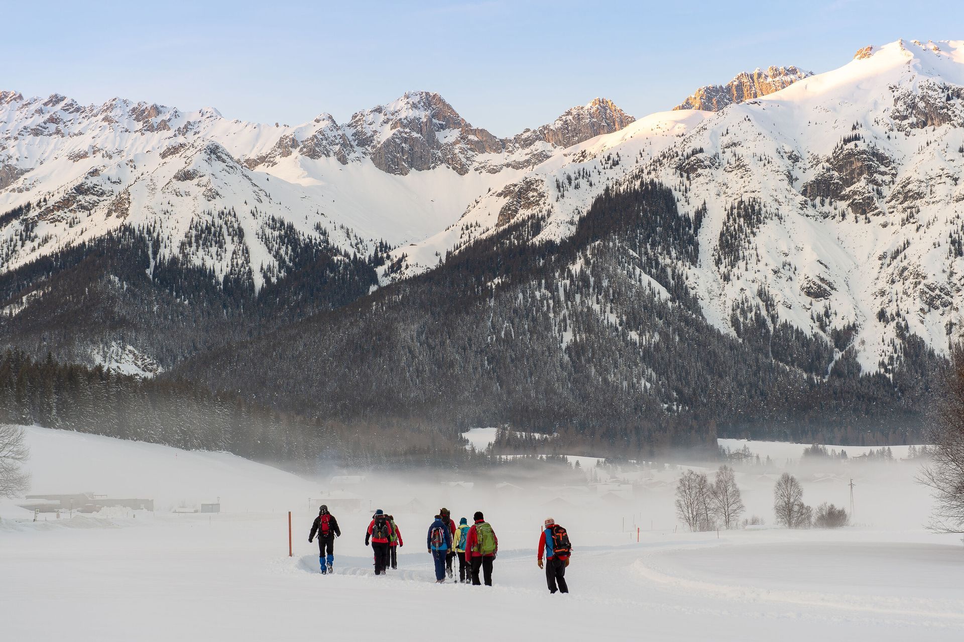 A group of people are walking through a snowy field with mountains in the background