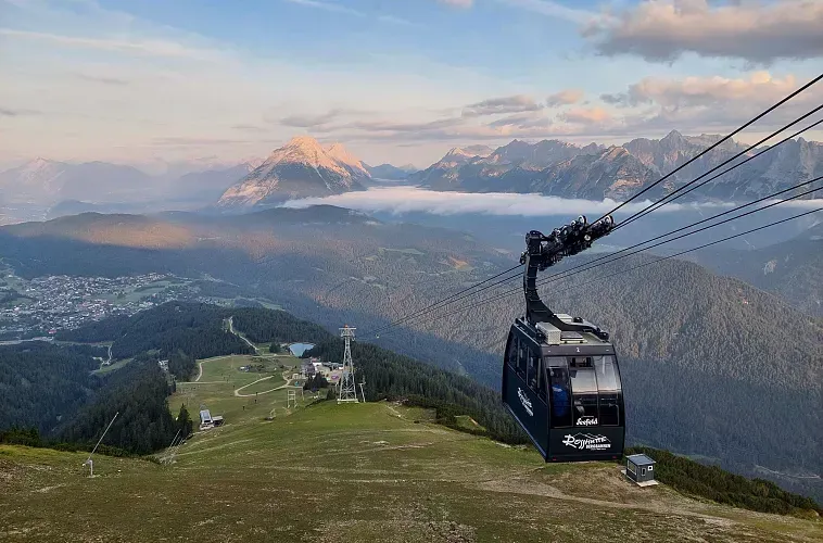 Eine Seilbahn fährt einen Berg hinunter, im Hintergrund sind Berge zu sehen.