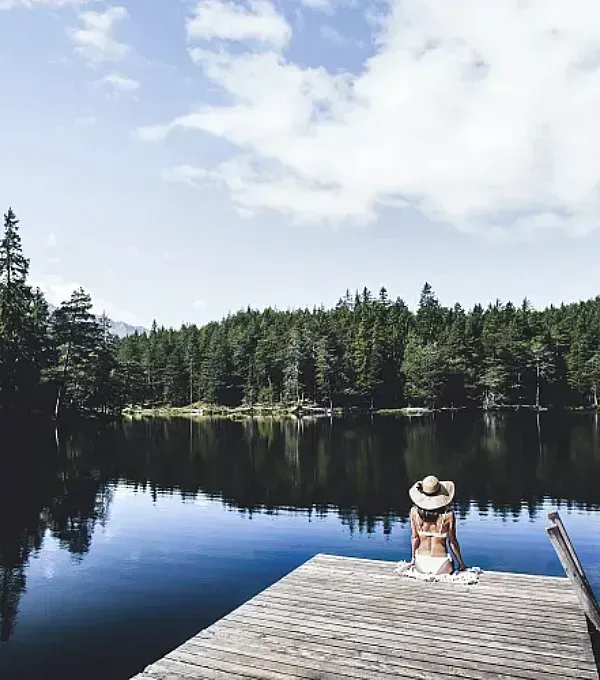Eine Frau sitzt auf einem Steg und blickt auf einen See.