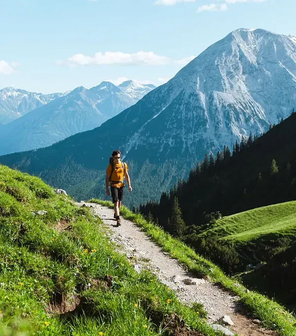 Eine Person geht einen Feldweg in den Bergen entlang.