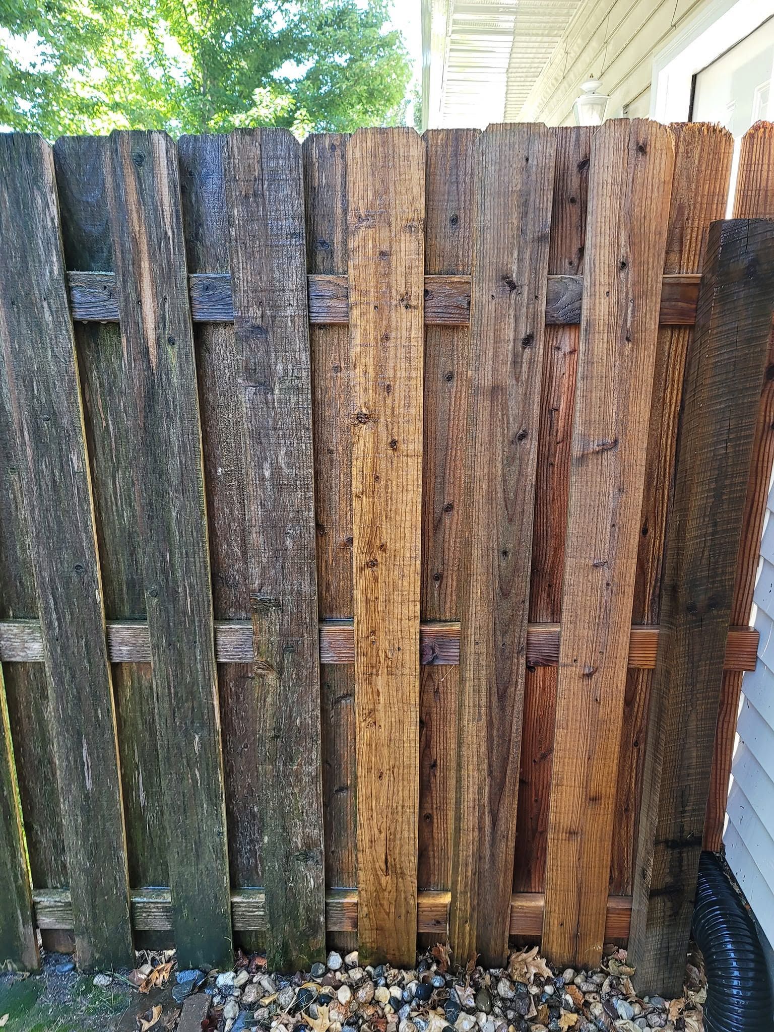 Weathered wooden fence panels in mixed gray and brown tones beside a house and greenery