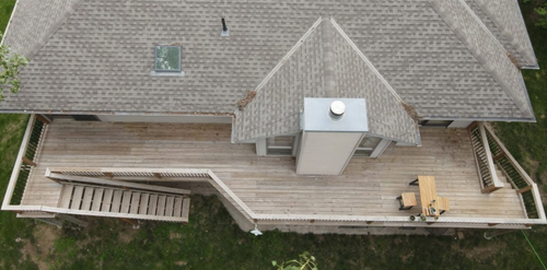 Aerial view of a house roof with a wooden deck, stairs, and outdoor chairs below.