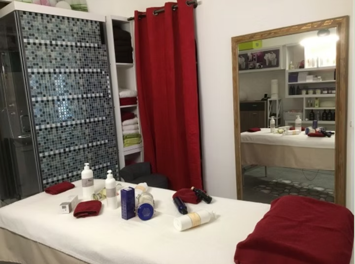 Salle de soins spa avec table de massage, rideaux rouges, serviettes pliées et grand miroir mural.