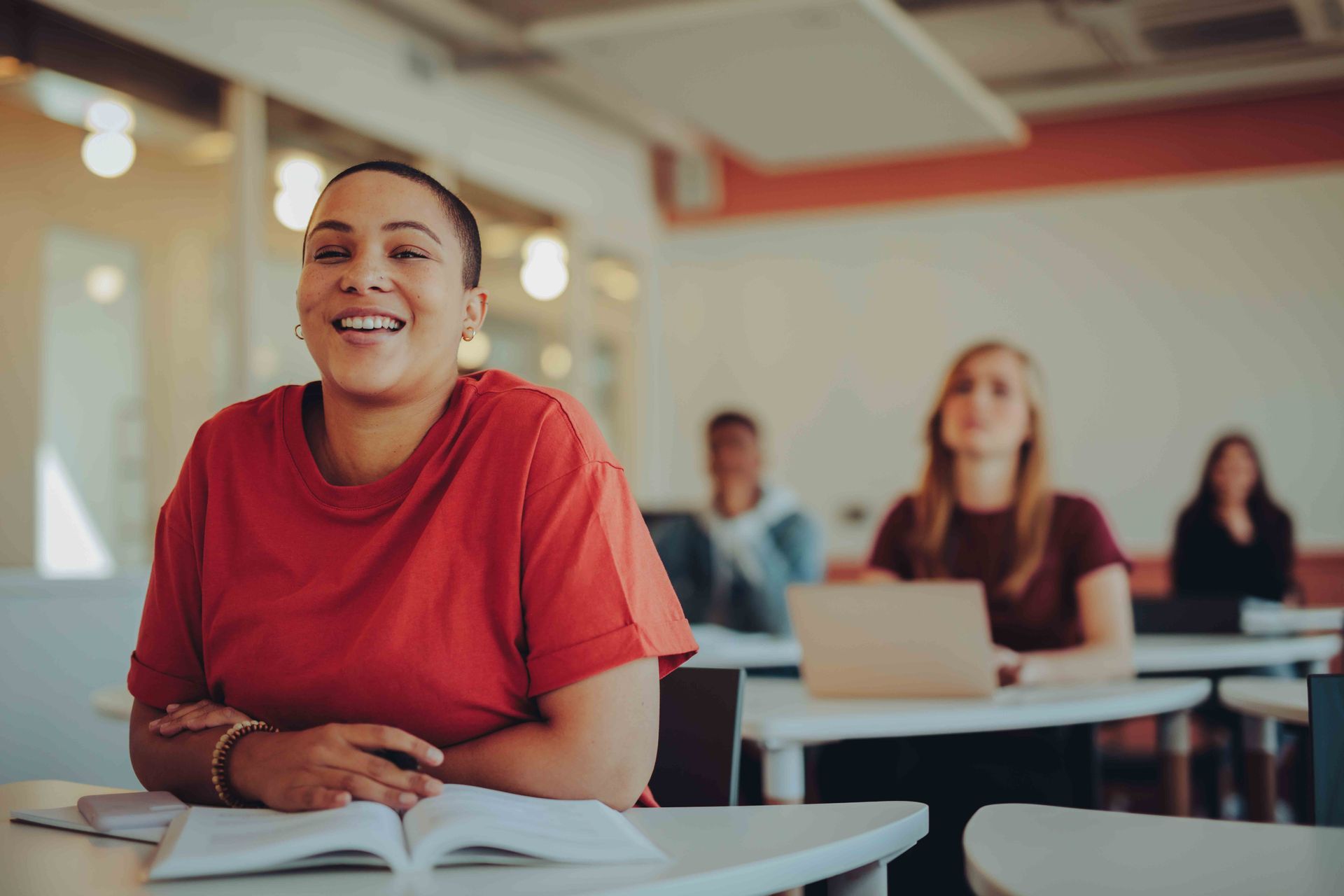A woman is smiling while sitting at a desk in a classroom.