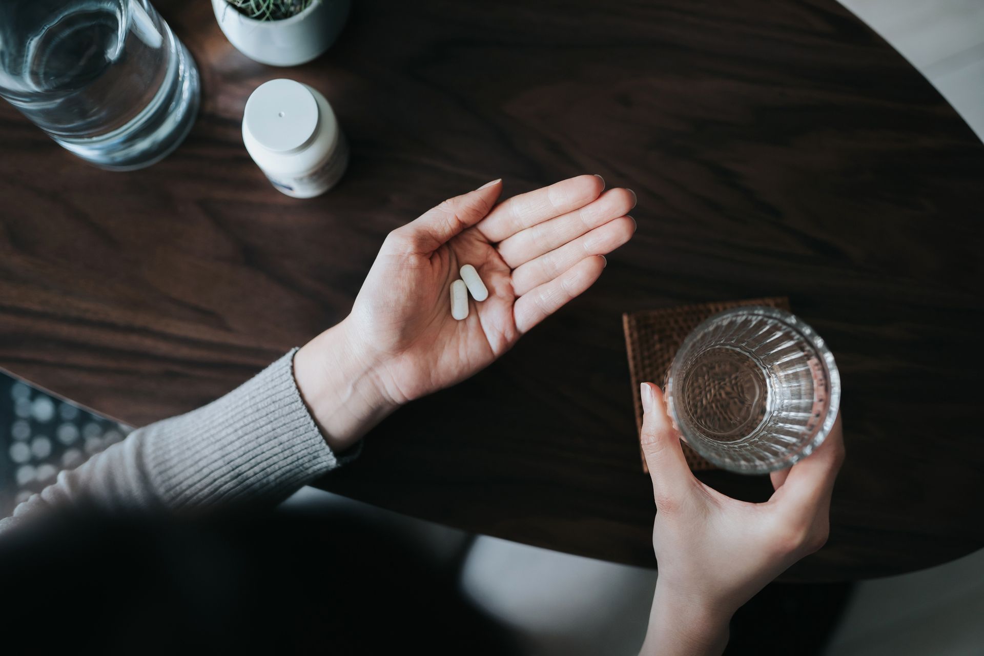 A woman is holding a glass of water and a pill in her hand.