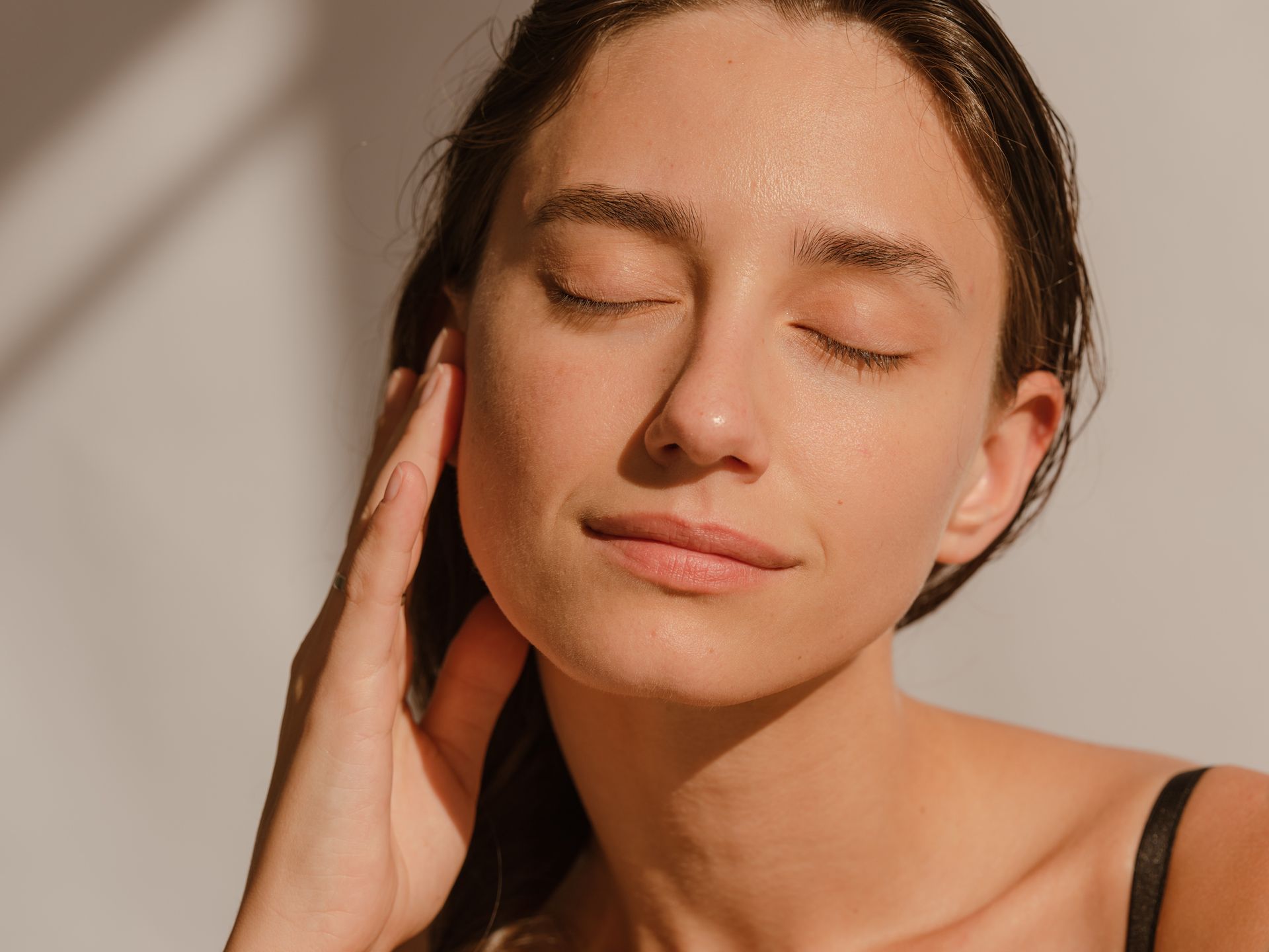 A woman is touching her face with her hand and her eyes closed.