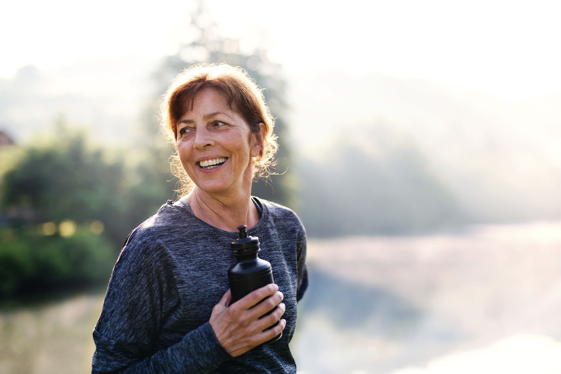 A woman is holding a water bottle and smiling.