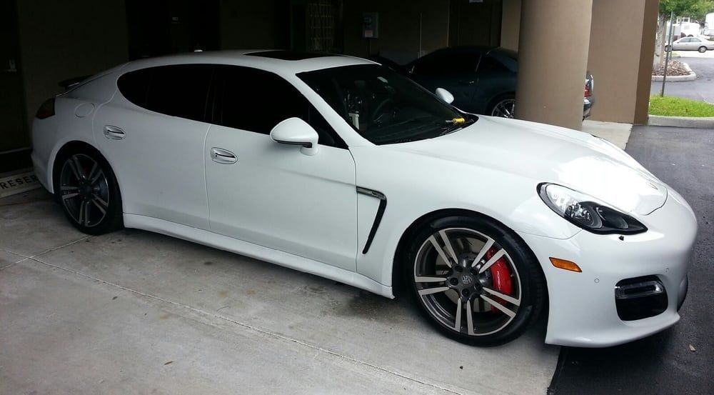 White Porsche Panamera parked under a covered area, with tinted windows and black rims.