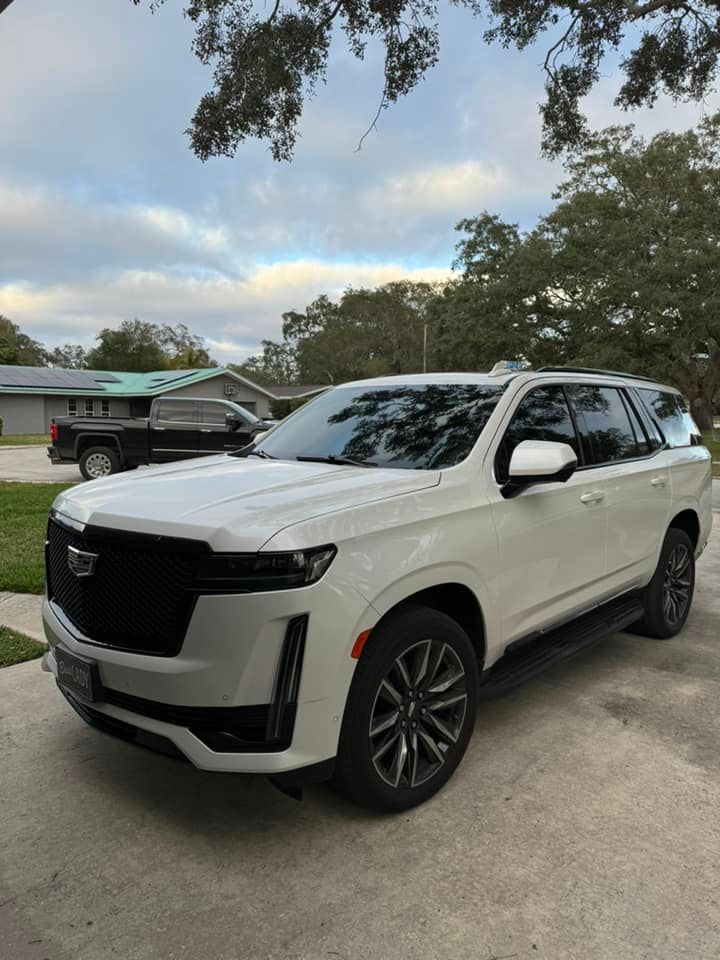 White Cadillac Escalade SUV parked in a driveway on a cloudy day.