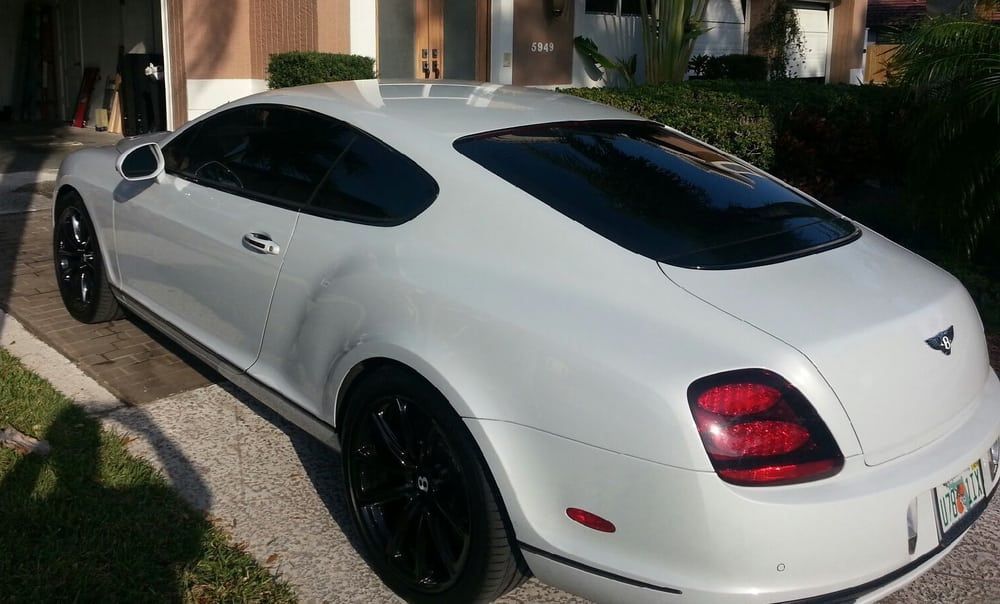 White Bentley coupe parked in a driveway; black wheels, tinted windows.
