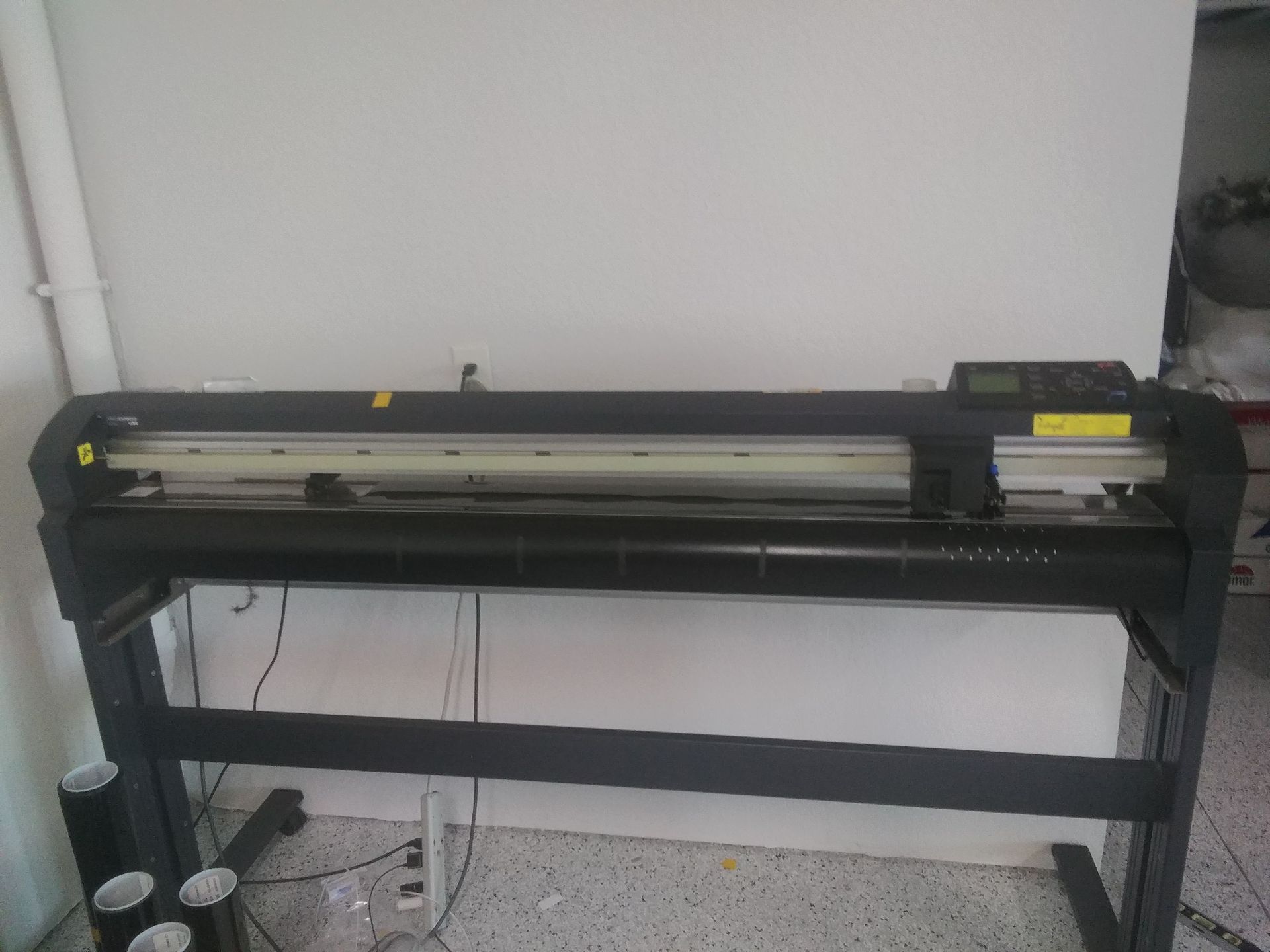 A black vinyl cutter machine on a stand against a white wall.