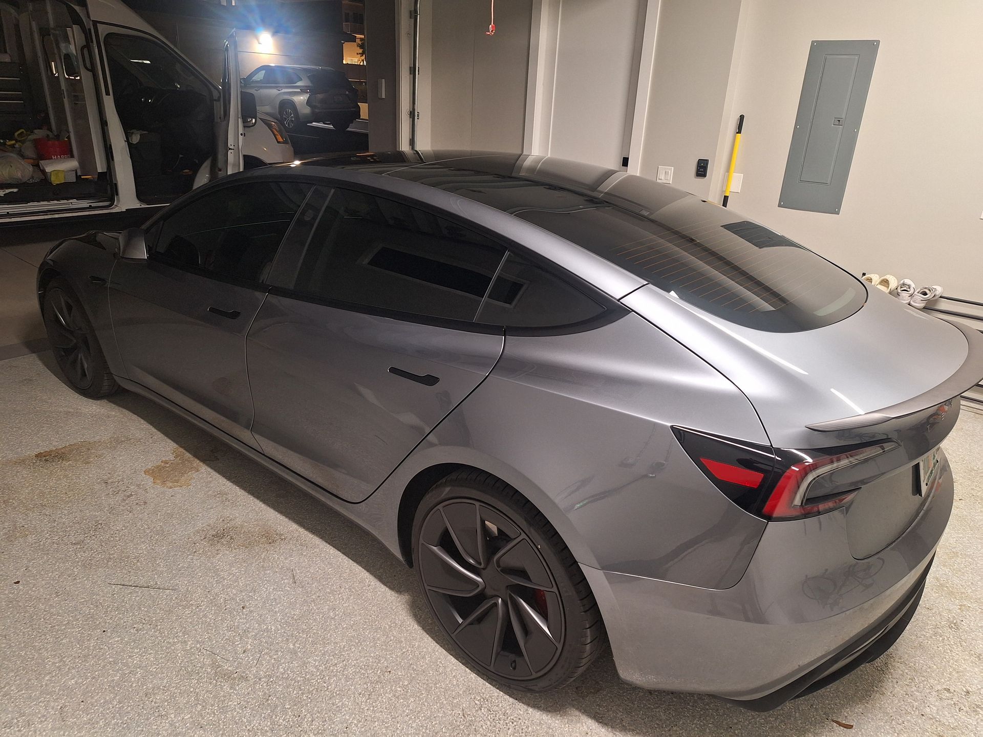 Gray Tesla Model 3 car parked inside a garage, with tinted windows and black wheels.