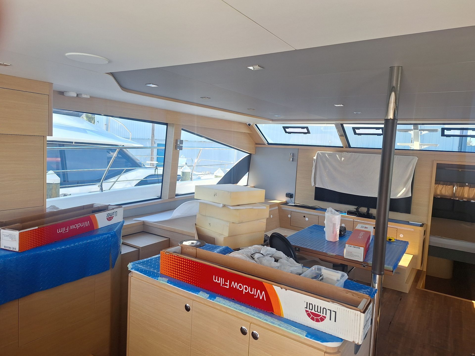 Interior of a boat with windows, boxes, and building materials; natural light illuminates the space.