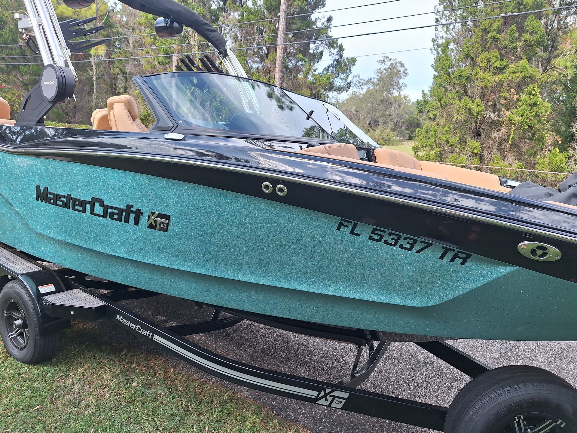 A teal and black MasterCraft boat on a trailer, with tan seating and a black tower.
