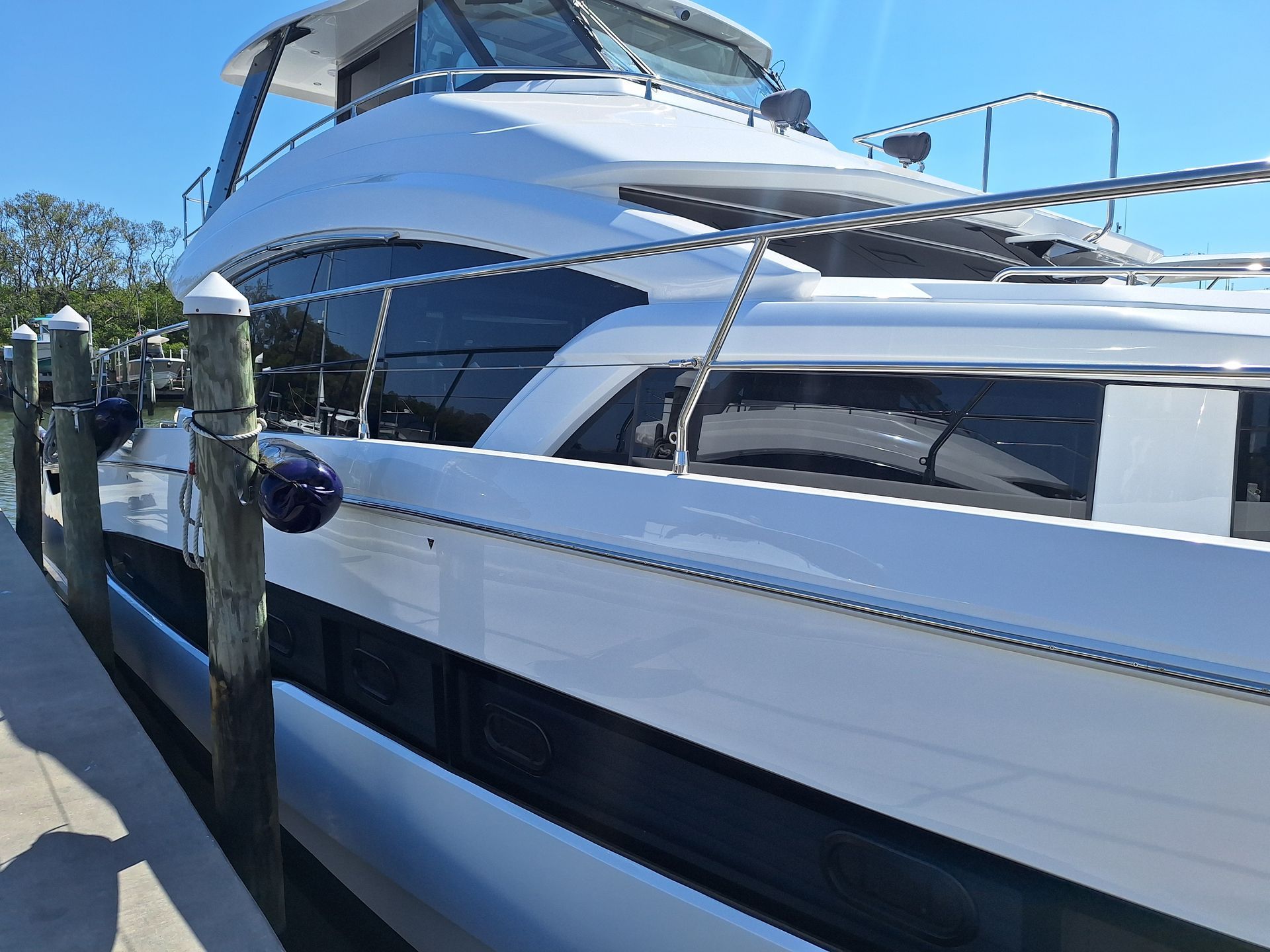 White and black yacht docked at a pier, blue sky.
