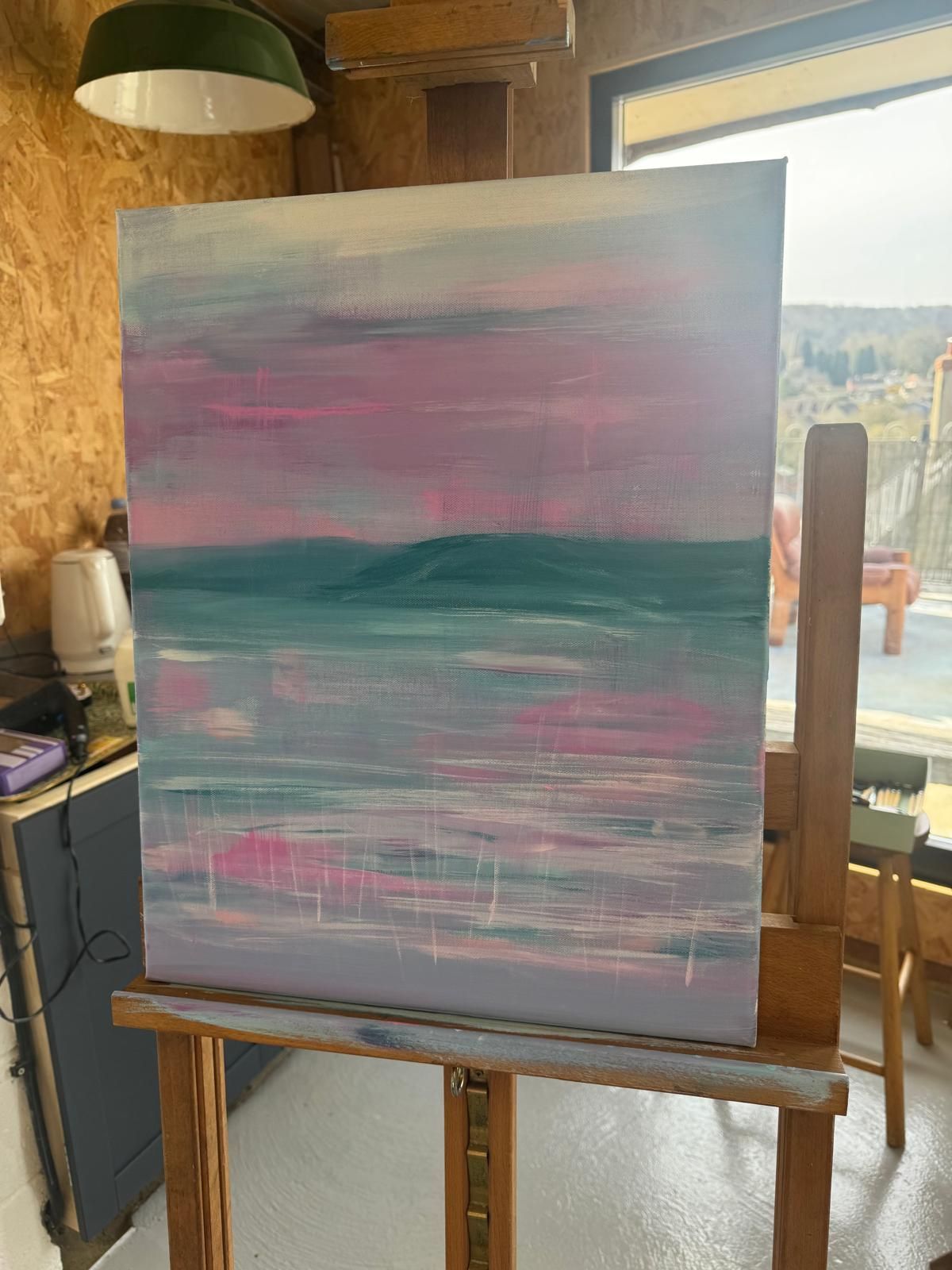Abstract landscape painting on an easel, with pink and teal hues.