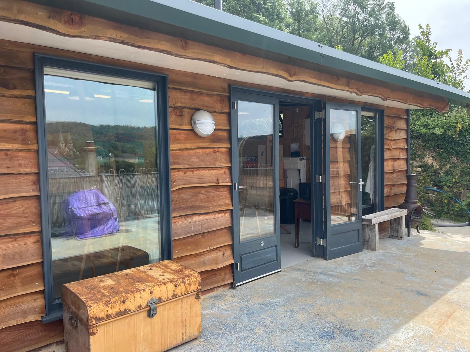 Art By Jemsy Studo  with large windows and doors, a weathered chest, and bench outside.