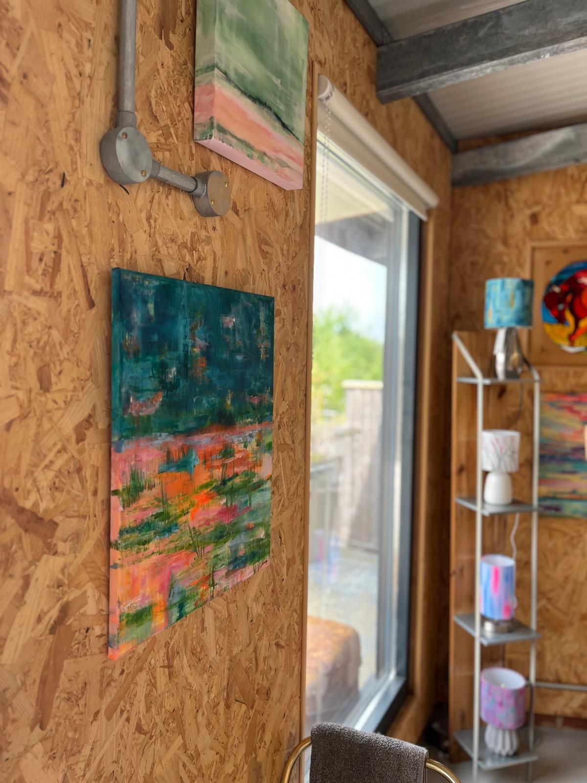 Artwork on a wood wall next to a window, with a metal shelf holding lamps.