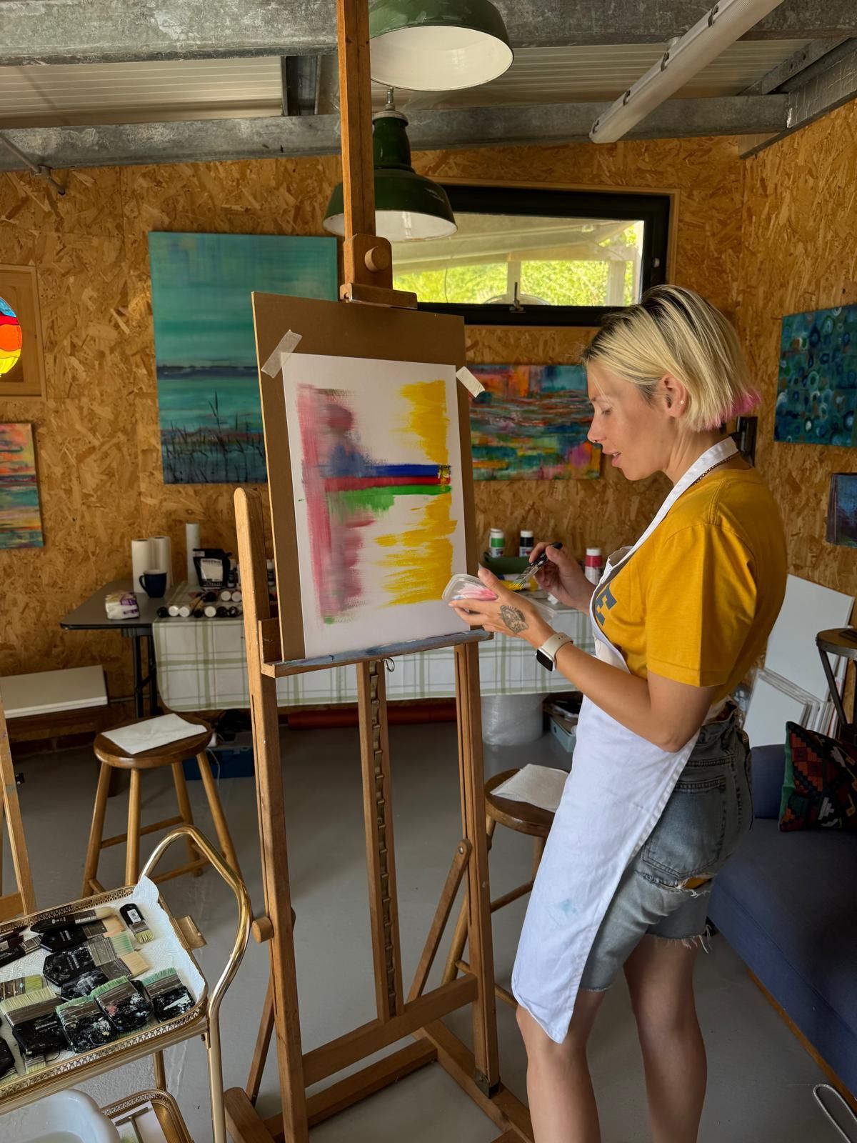 Workshop customer painting an abstract work in a bright studio. She wears a yellow shirt and an apron.