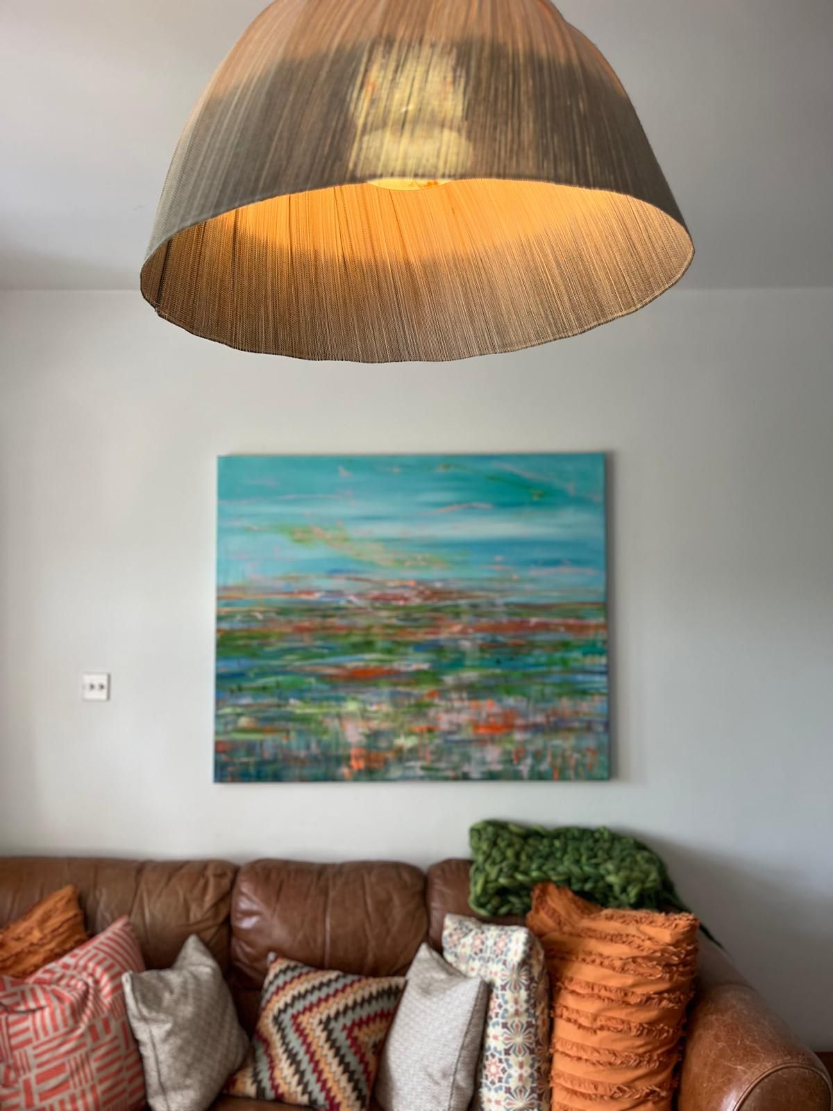 Living room with leather sofa, colorful pillows, abstract painting, and woven lamp shade.