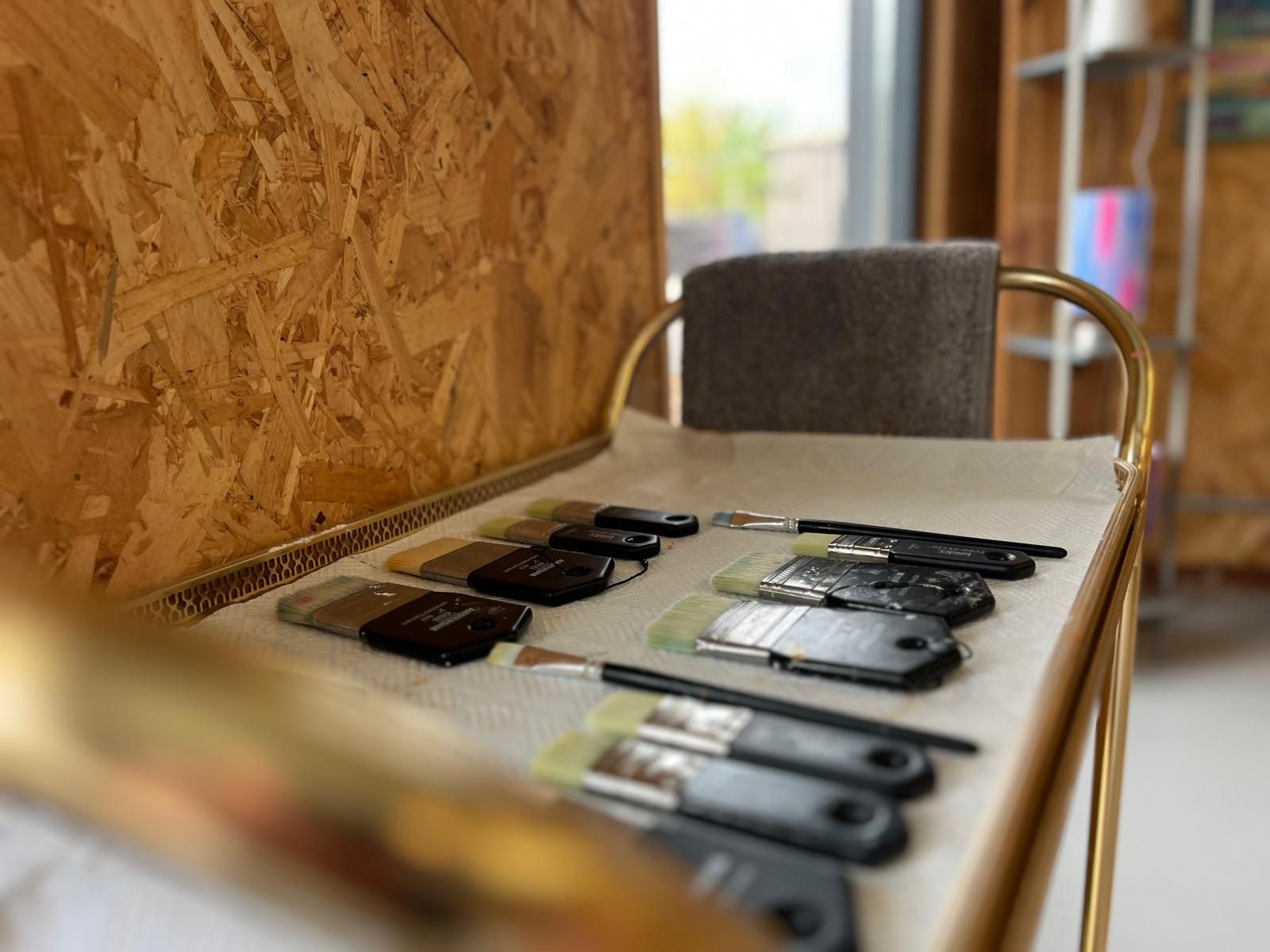Paintbrushes lined up on a tray, ready for use, inside a brightly lit art studio.