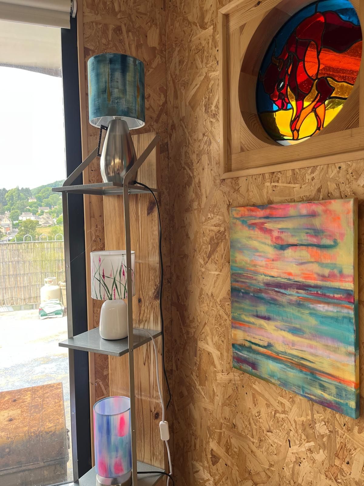 A corner with a lamp shelf, art, and a stained glass window against wood paneling.