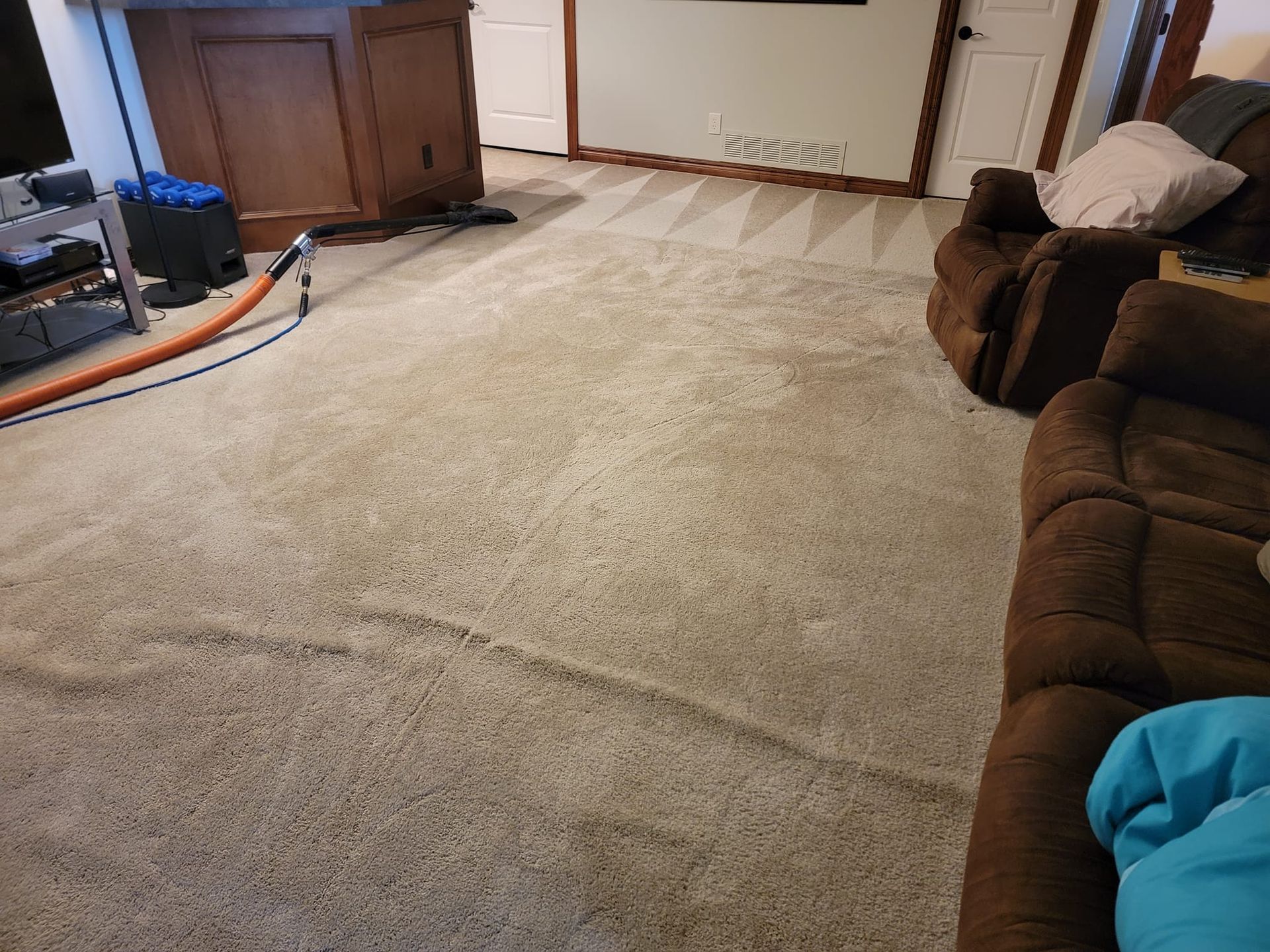 A living room with a couch and two chairs and a vacuum cleaner on the floor.