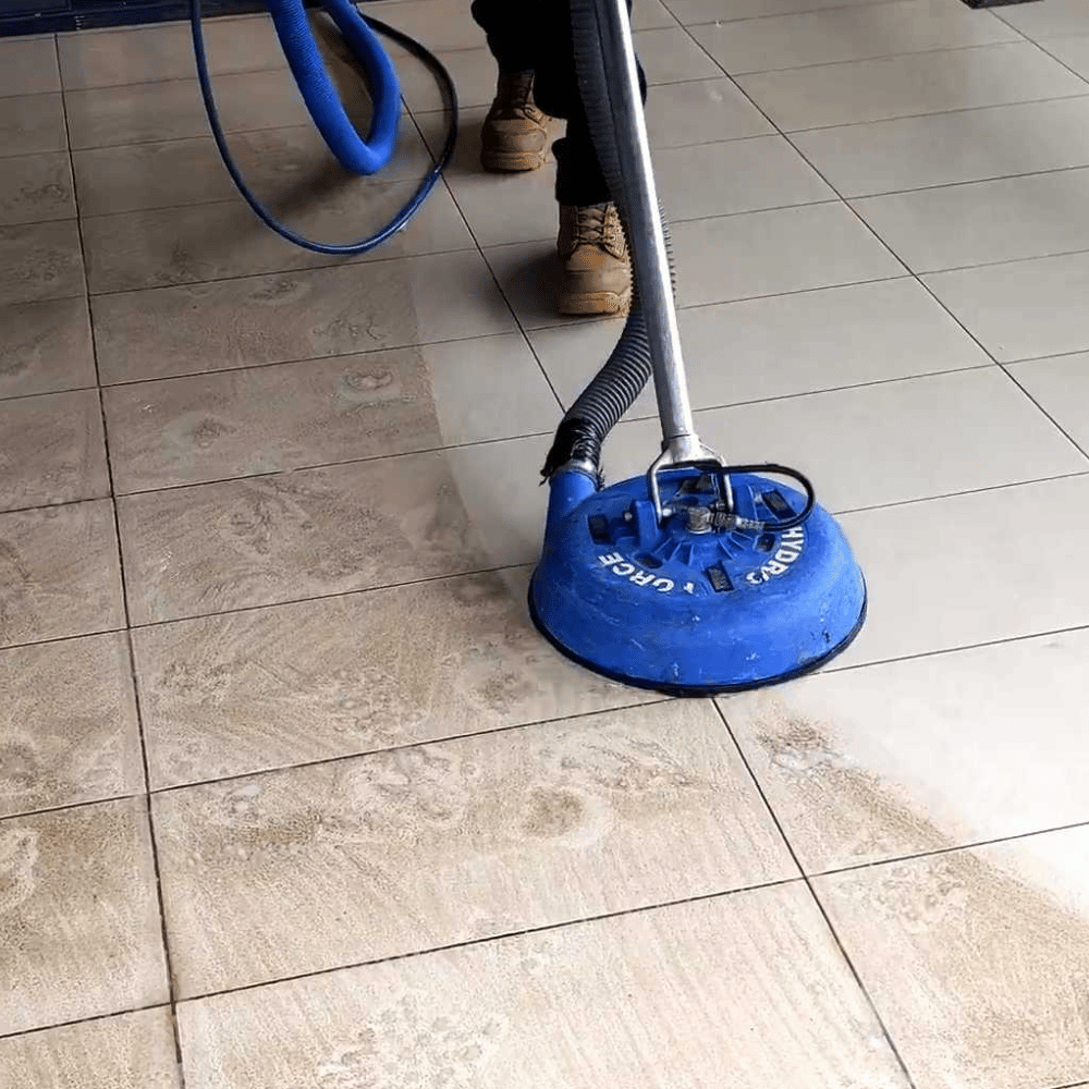 Person wearing pink gloves scrubbing white bathroom tiles with a green and white brush.