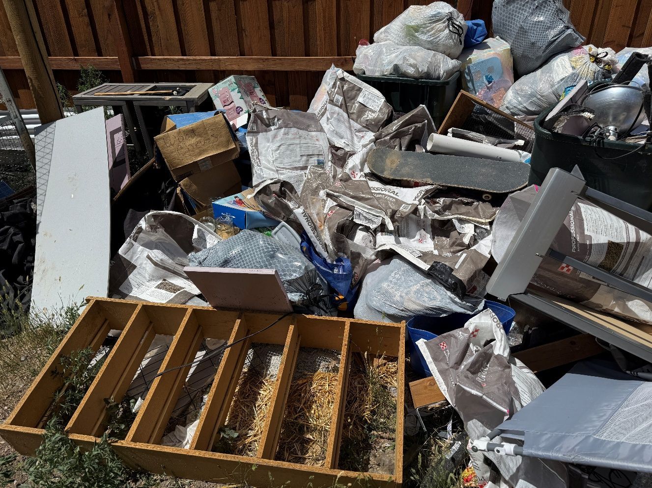 Person holding open black trash bag outdoors, wearing plaid shirt and gloves.