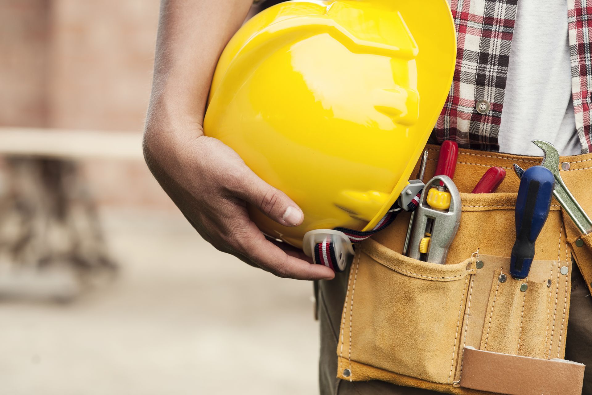 A construction worker is holding a hard hat and a tool belt.