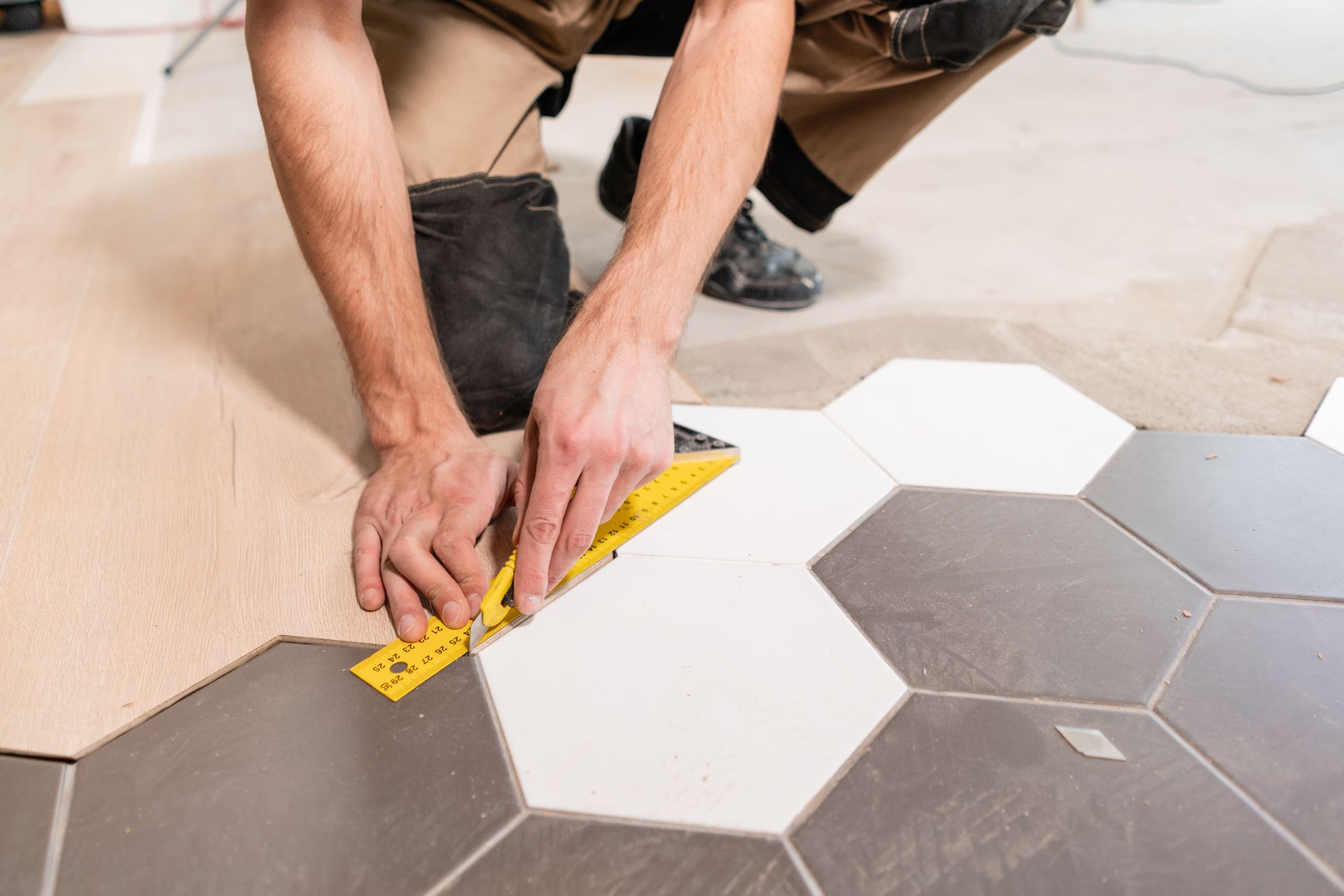 A man is measuring a tile floor with a ruler.