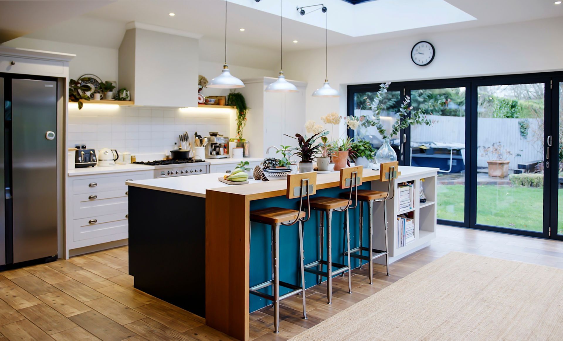 A kitchen with a large island and stools and a clock on the wall.