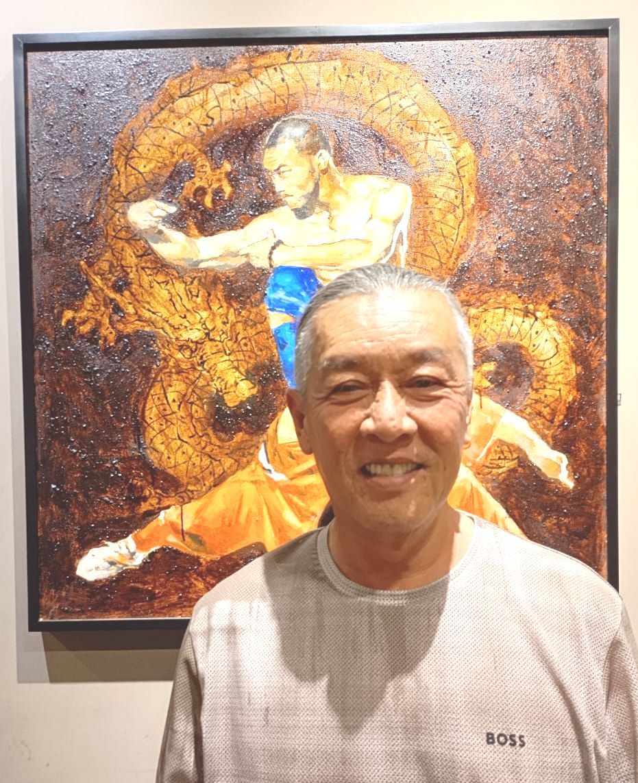 A man is standing in front of a painting of a man fighting a dragon.
