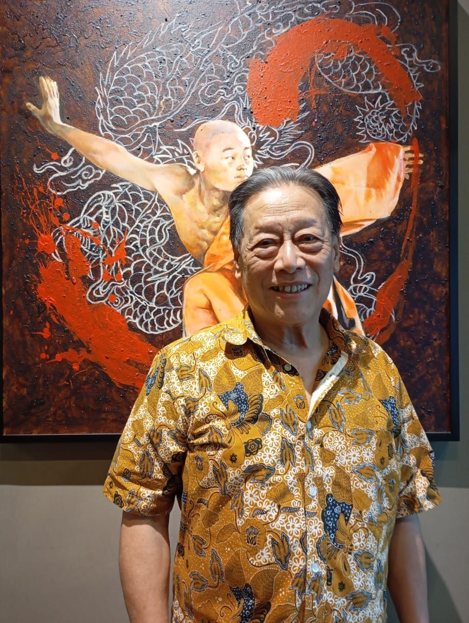A man in a yellow shirt is standing in front of a painting.