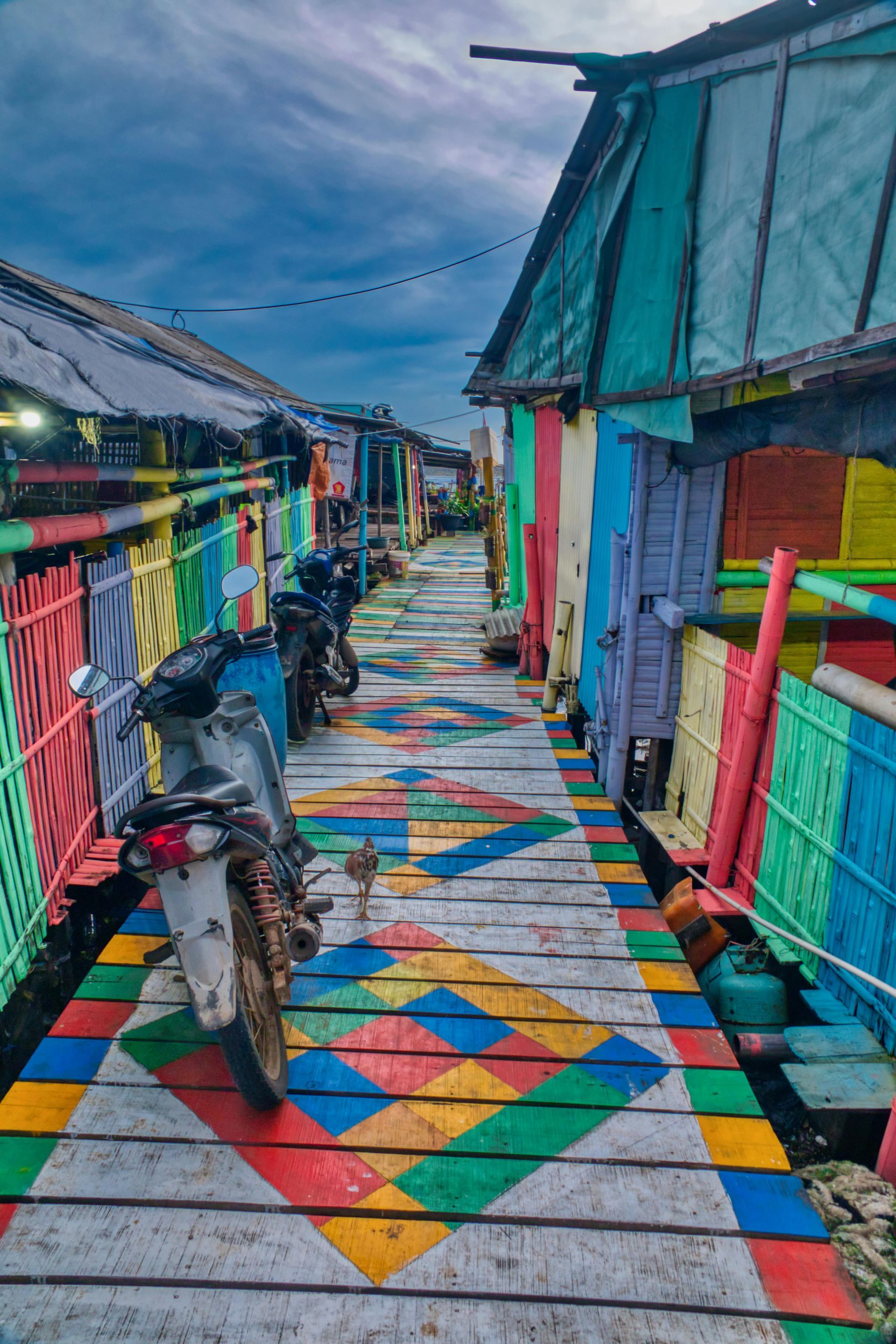 A motorcycle is parked on a wooden walkway between colorful houses.