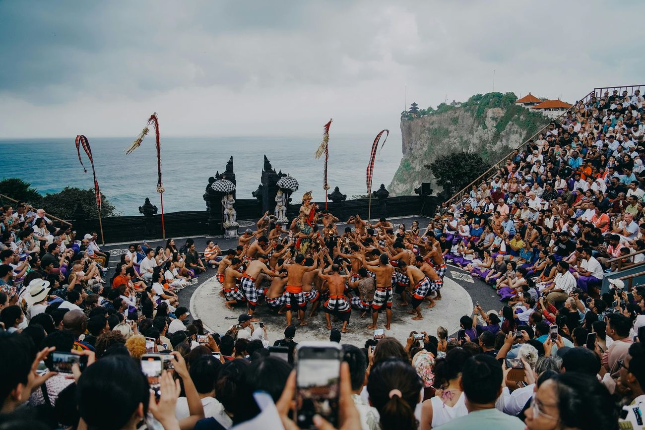 A crowd of people are watching a performance on a stage in front of the ocean.
