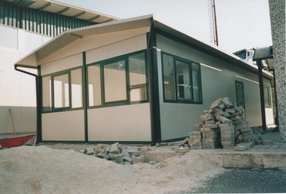 Edificio prefabbricato con finestre con finiture verdi, tetto curvo e materiali da costruzione nella parte anteriore.