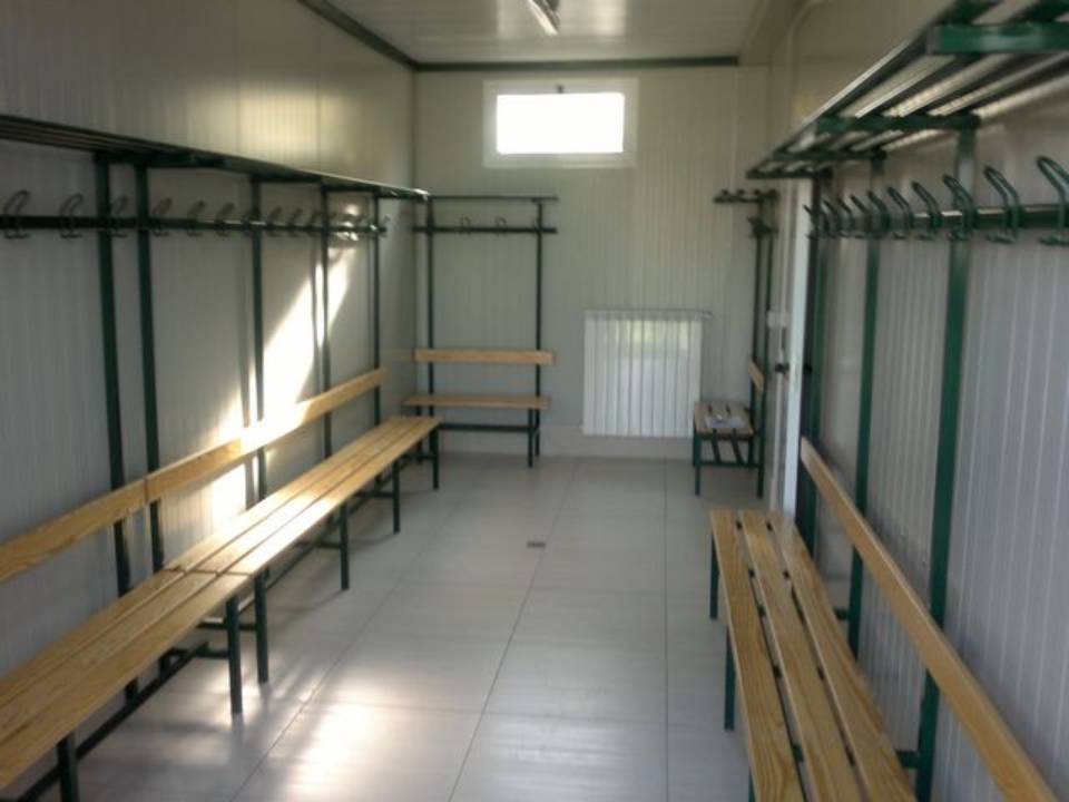 Spogliatoio vuoto con panche, attaccapanni e una piccola finestra.