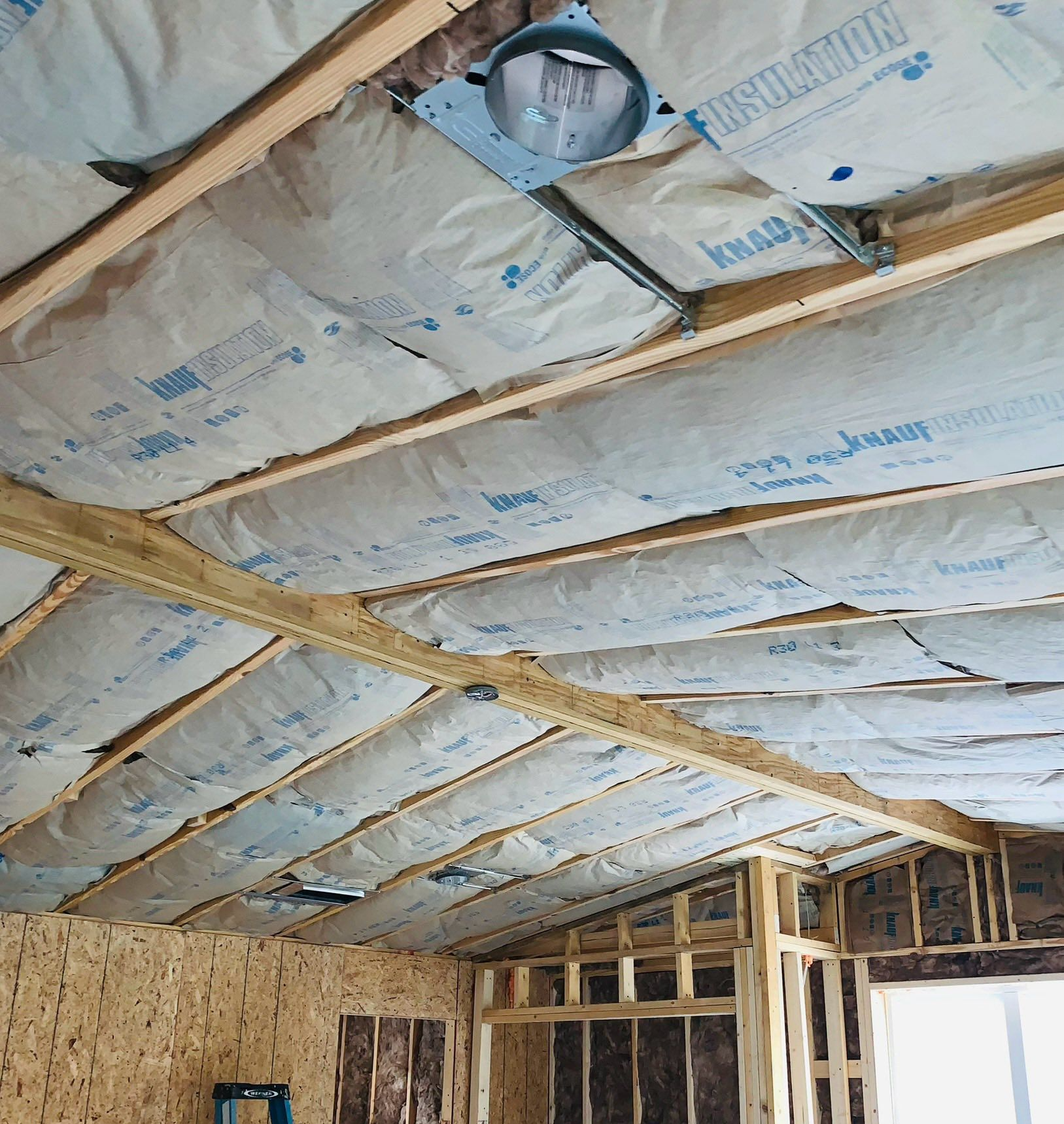 Interior view of a room under construction with exposed wood framing and insulation installed in the ceiling.