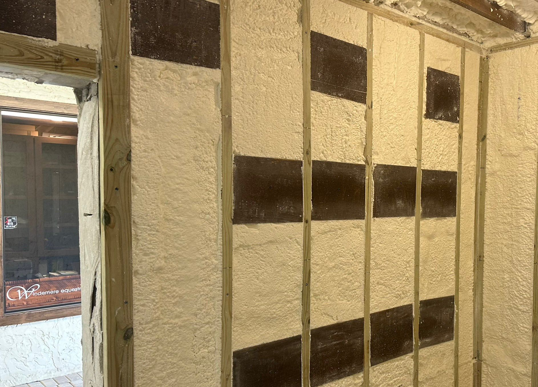 Interior wall with spray foam insulation, dark rectangles, and wooden framing.
