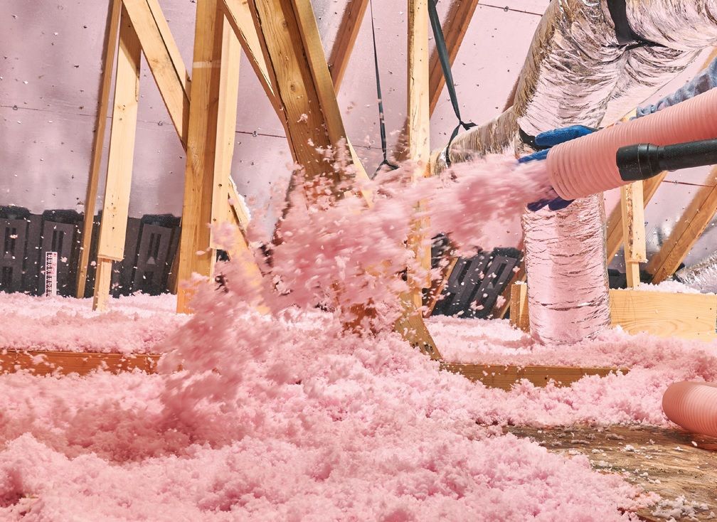 Person installing pink fiberglass insulation in a wooden wall frame.