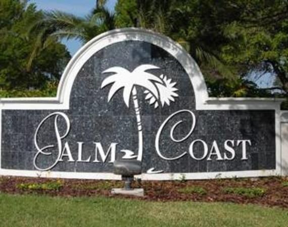 Sign for Palm Coast with white text and palm tree silhouette on a dark stone background.